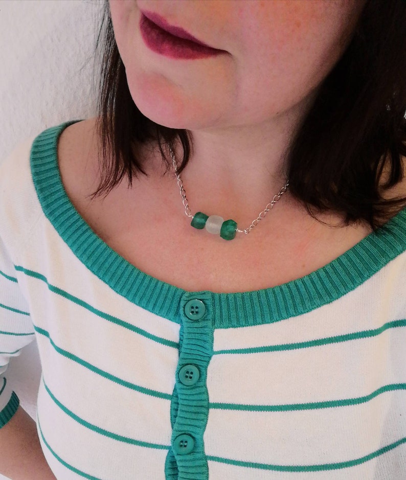 Peut inclure: Un collier en cha&icirc;ne argent avec trois perles en verre vert et blanc. Le collier est port&eacute; par une personne aux cheveux fonc&eacute;s et portant une chemise &agrave; rayures vertes et blanches.