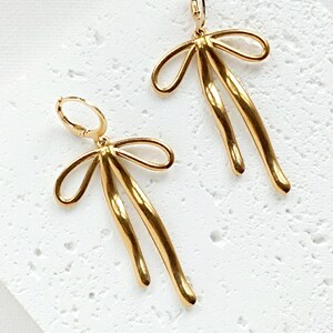May include: A pair of gold-toned earrings with a bow design. The earrings are made of metal and have a hoop closure.