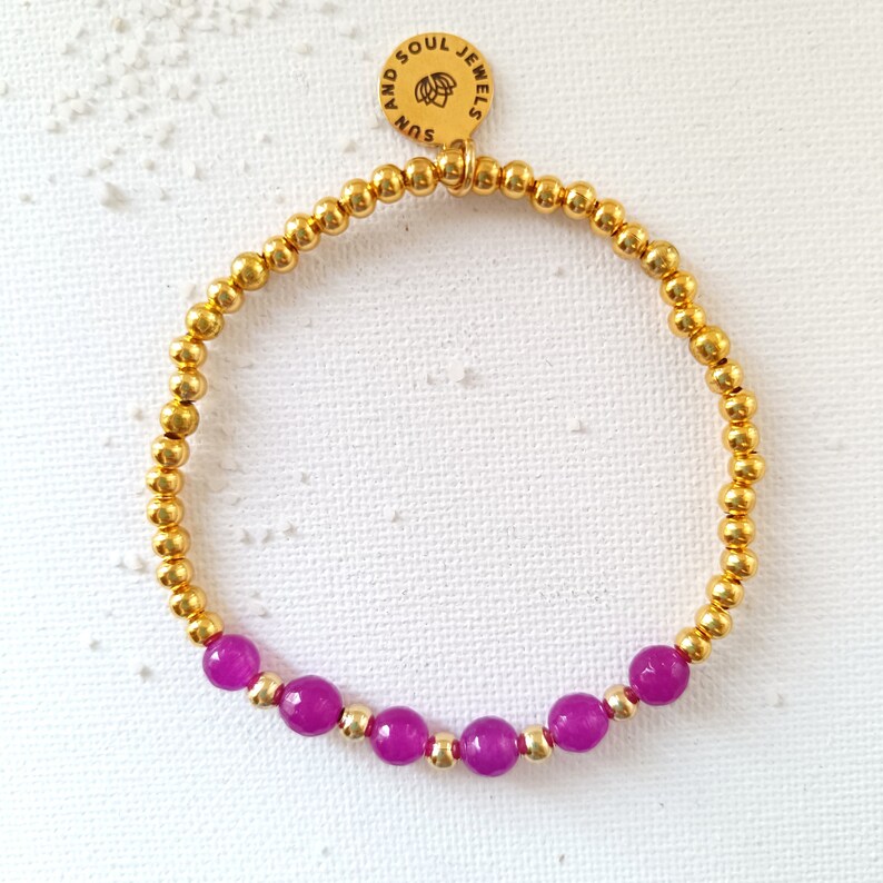 May include: A gold beaded bracelet with a charm that says "Sun and Soul Jewels". The bracelet has a row of purple beads.