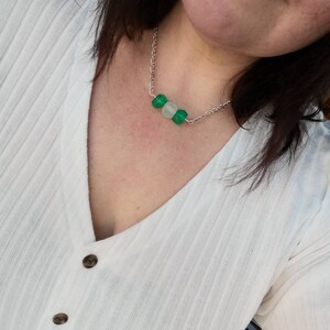 Peut inclure: Un collier en cha&icirc;ne argent avec trois perles rondes. Les perles sont vertes et blanches.