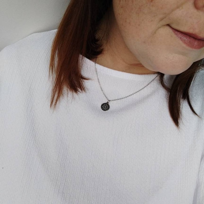 May include: A silver chain necklace with a small, round pendant featuring a detailed, stylized sun design.