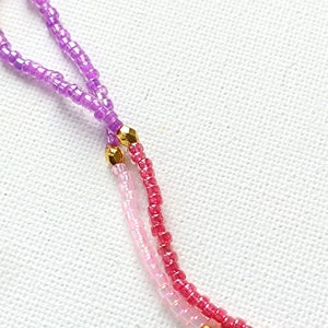 Puede incluir: Primer plano de un collar de cuentas multicolores con detalles dorados. El collar est&aacute; hecho de peque&ntilde;as cuentas redondas en tonos de morado, rosa y rojo.
