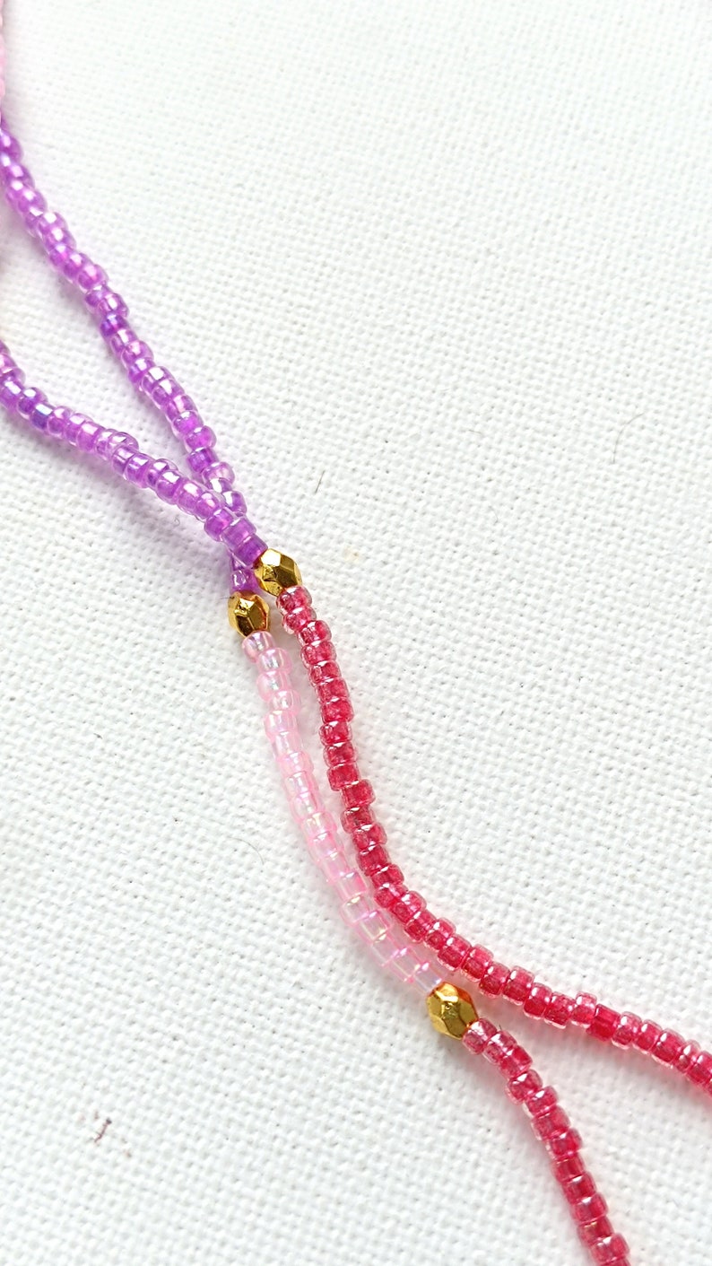 Puede incluir: Primer plano de un collar de cuentas multicolores con detalles dorados. El collar est&aacute; hecho de peque&ntilde;as cuentas redondas en tonos de morado, rosa y rojo.