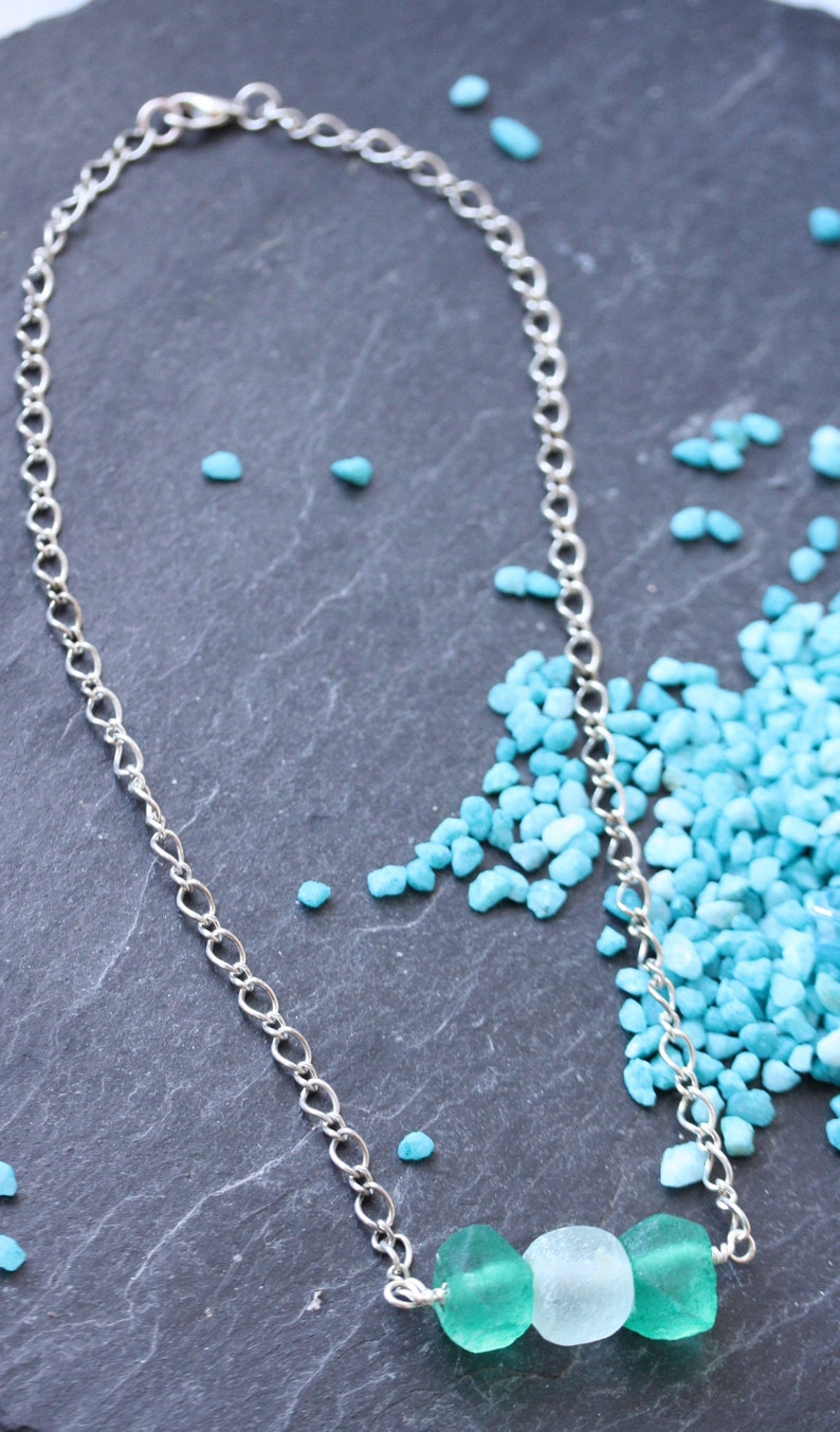Peut inclure: Un collier en cha&icirc;ne argent avec trois perles en verre turquoise. Les perles sont un m&eacute;lange de turquoise clair et fonc&eacute;.