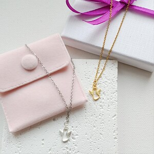 May include: Two silver angel necklaces with a delicate chain and a small angel pendant. One necklace is in a pink velvet pouch, the other is on a white surface.