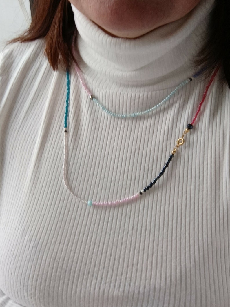 May include: A layered necklace with pink, blue, and black beads. The necklace has a gold clasp and a single turquoise bead.