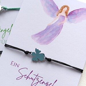Peut inclure: Un bracelet en cordon noir avec un charm en forme de tr&egrave;fle &agrave; quatre feuilles de couleur turquoise. Le bracelet est pr&eacute;sent&eacute; sur une carte avec une illustration &agrave; l'aquarelle d'un ange et le texte "EIN Schutzengel F&Uuml;R DICH".