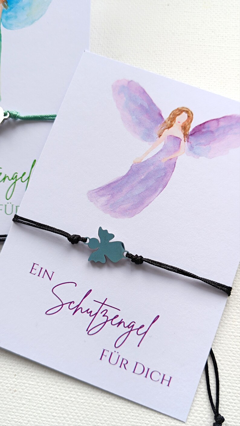 Peut inclure: Un bracelet en cordon noir avec un charm en forme de tr&egrave;fle &agrave; quatre feuilles de couleur turquoise. Le bracelet est pr&eacute;sent&eacute; sur une carte avec une illustration &agrave; l'aquarelle d'un ange et le texte "EIN Schutzengel F&Uuml;R DICH".