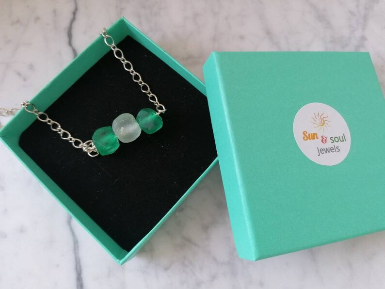 Peut inclure: Un collier en cha&icirc;ne argent&eacute;e avec trois perles en verre vert et blanc. Le collier est dans une bo&icirc;te cadeau turquoise avec le logo "Sun & Soul Jewels".