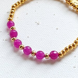 May include: A gold bracelet with pink beads and a gold charm with the word "SUN" on it.