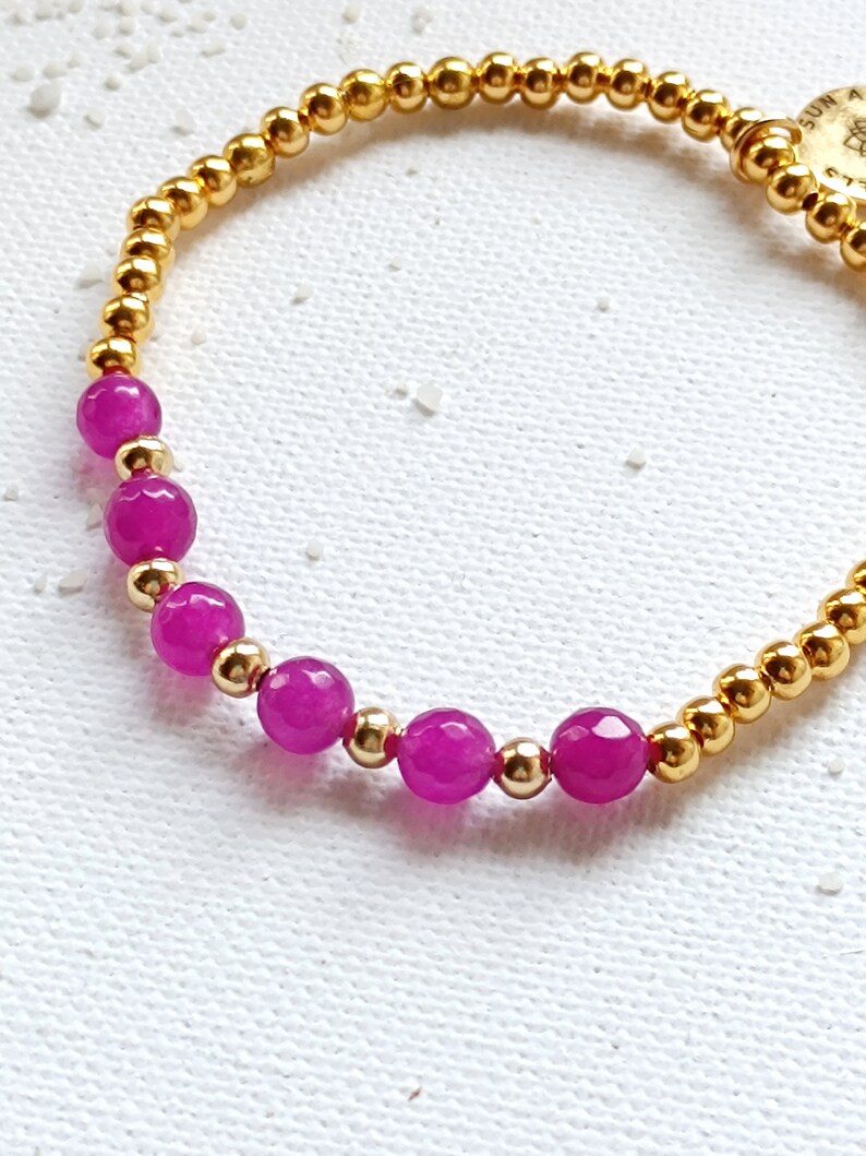 May include: A gold bracelet with pink beads and a gold charm with the word "SUN" on it.