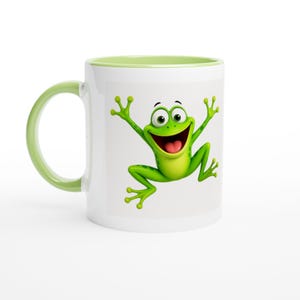 Könnte beinhalten: Ein weißer Keramikbecher mit einer leuchtend grünen Froschgrafik, die ein breites, fröhliches Lächeln zeigt und die Arme hebt. Der Becher hat einen hellgrünen Henkel und einen passenden hellgrünen Rand, was einen farblichen Kontrast bildet.