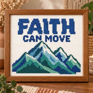 May include: A framed cross-stitch embroidery featuring the text FAITH CAN MOVE in bold blue letters above a stylized mountain range rendered in various shades of blue, teal, and green on a white fabric background, enclosed in a wooden frame.