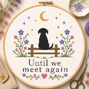 May include: A circular wooden embroidery hoop containing a cross-stitch pattern of a black dog sitting on a brown fence under a yellow crescent moon and stars. The text "Until we meet again" is stitched in black, surrounded by colorful floral motifs.