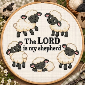 May include: A circular wooden embroidery hoop containing a cross-stitch pattern on white fabric. The design features five small sheep with black faces and white wool, surrounding the black stitched text, The LORD is my shepherd.