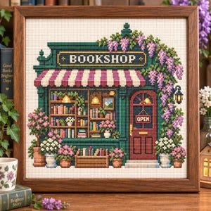 May include: A framed cross-stitch embroidery depicting a bookstore storefront with a dark green facade, a striped awning, and shelves filled with books. The shop features a red door with an OPEN sign, surrounded by purple wisteria and potted flowers.