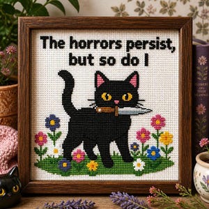 Peut inclure: Une broderie au point de croix encadrée représentant un chat noir tenant un couteau dans sa gueule, debout dans un champ de fleurs colorées. Le texte au-dessus du chat indique : "The horrors persist, but so do I." Cadre en bois brun foncé.