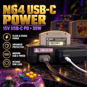 May include: A black Nintendo 64 game console with a grey game cartridge inserted. The console features a white USB-C power cable connected to the side. Text on the image reads N64 USB-C POWER, 15V USB-C PD 30W, CLEAN & STABLE POWER, ADVANCED PROTECTION, MODERN USB-C POWER, RETAINS OEM LOOK.