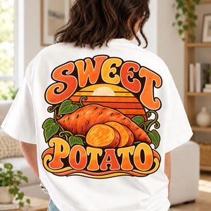 Może przedstawiać: Biały t-shirt z dużą grafiką na plecach. Wzór przedstawia słodkiego ziemniaka z zielonymi liśćmi na tle zachodzącego słońca z pomarańczowymi i żółtymi pasami. Napis "SWEET POTATO" został wydrukowany pogrubioną czcionką w stylu retro.