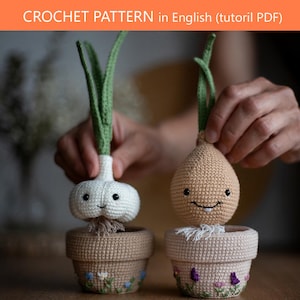 May include: Two crocheted amigurumi vegetables, a white garlic bulb and a tan onion, each with green stalks and embroidered faces, sitting in small tan crocheted pots with floral embroidery. Text reads: CROCHET PATTERN in English (tutoril PDF).