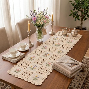 May include: A rectangular table runner featuring alternating squares of cream-colored fabric with embroidered floral motifs and intricate beige crochet lace patterns. The runner has a scalloped edge and is displayed on a wooden table with tea sets.