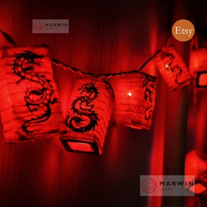 May include: A string of red paper lanterns, each featuring a black dragon motif. The lanterns are illuminated, producing a warm, ambient light. The Etsy logo is visible. The Marwin Craft logo is also visible.
