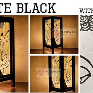 May include: A black wooden table lamp with a white and gold Buddha face design. The lamp is lit and the light shines through the paper. The lamp is on a wooden table. The lamp is made by Marwin Craft. The lamp is available on Etsy.