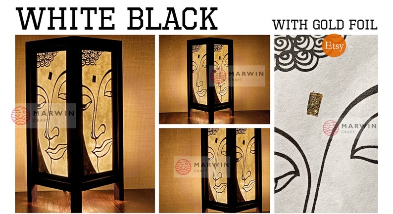 May include: A black wooden table lamp with a white and gold Buddha face design. The lamp is lit and the light shines through the paper. The lamp is on a wooden table. The lamp is made by Marwin Craft. The lamp is available on Etsy.