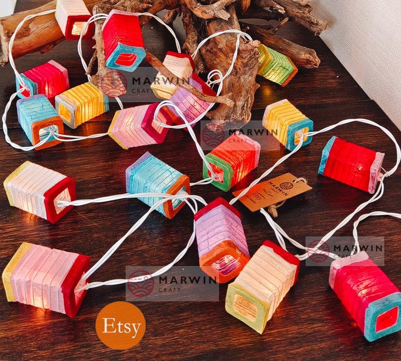May include: A string of colorful paper lanterns with lights inside. The lanterns are made of thin paper and have a square shape. The lights are white and create a warm glow. The lanterns are strung together with white wire. The text "MARWIN CRAFT" is visible on the image. The text "Etsy" is visible on the image.