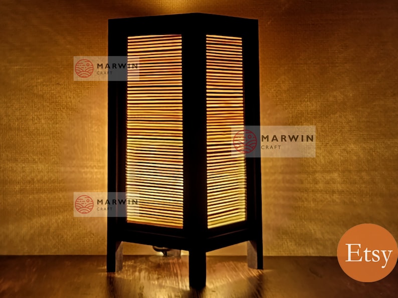 May include: A wooden table lamp with a slatted bamboo shade. The lamp is lit and casts a warm glow. The lamp is on a wooden surface. The text "Etsy" is visible in the lower right corner of the image.