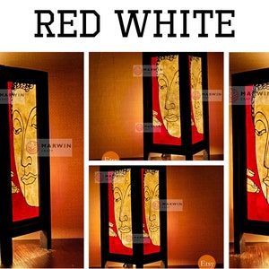 May include: A wooden table lamp with a red and white design featuring a Buddha face. The lamp is lit and has a warm glow.