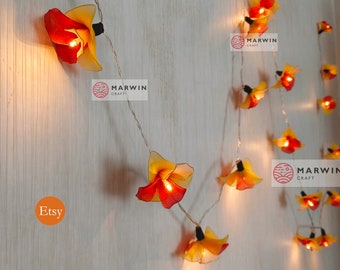 May include: String lights with yellow and red flower-shaped paper lanterns. The lights are strung on a clear wire and are hanging on a white wall. The text "MARWIN CRAFT" is visible on the wall. The text "Etsy" is also visible on the wall.