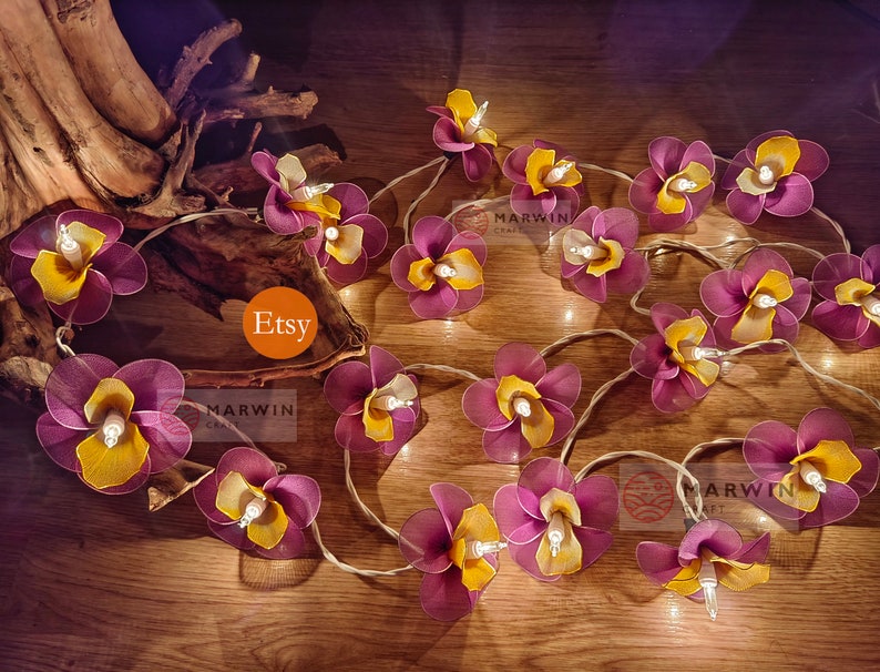 Puede incluir: Una cadena de luces con bombillas en forma de flores moradas y amarillas. Las luces est&aacute;n enhebradas en un cable transparente y est&aacute;n encendidas. Las flores est&aacute;n hechas de tela y tienen un aspecto delicado y femenino. Las luces son perfectas para a&ntilde;adir un toque de fantas&iacute;a y romanticismo a cualquier espacio.