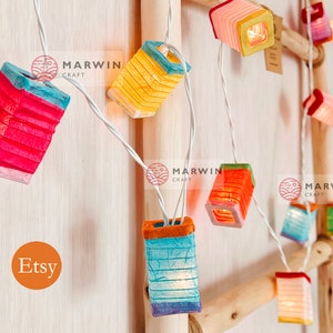 May include: String of lights with colorful paper lanterns. The lanterns are shaped like squares and have a white wire running through them. The lanterns are lit up and glowing. The text "Marwin Craft" is visible on the image.