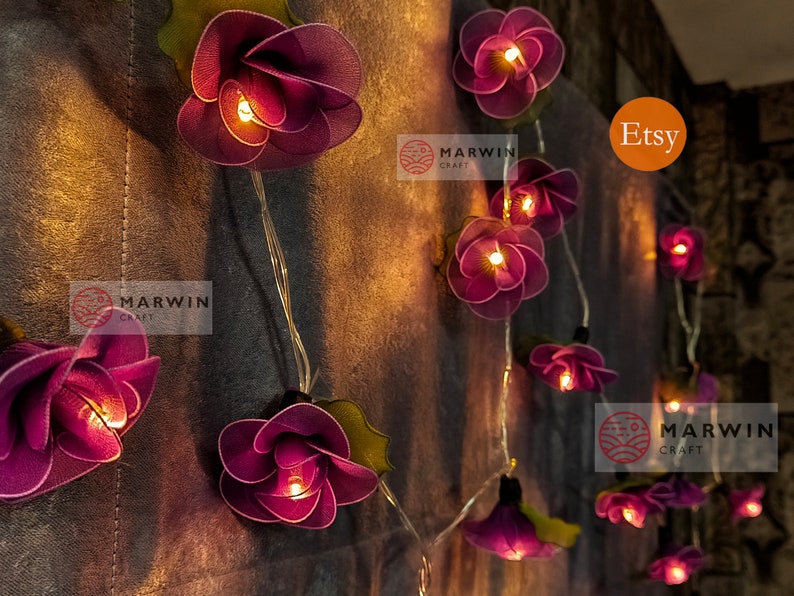 May include: String lights with purple fabric flowers, each with a warm white LED light inside. The lights are strung on a clear wire and are perfect for adding a touch of whimsy to any space. The lights are labeled "Marwin Craft" and "Etsy".