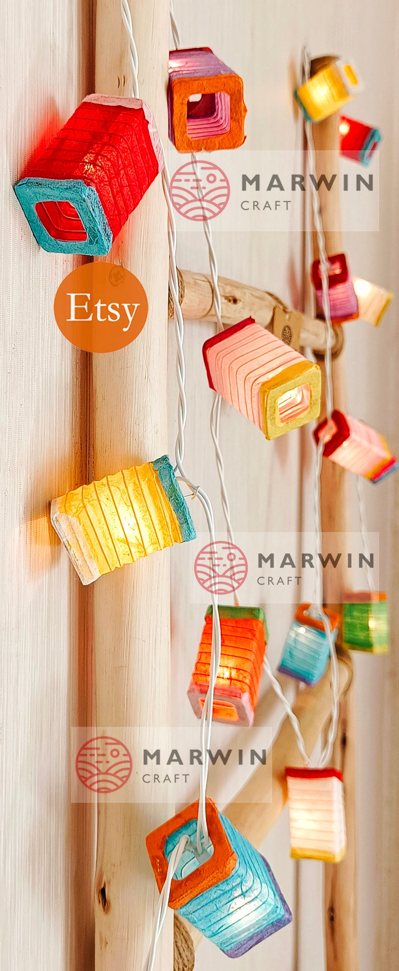 May include: String of colorful, illuminated paper lanterns. Each lantern is a small, square shape with a different color scheme, including red, orange, yellow, and blue. The lanterns are strung on a white wire, with the Etsy logo visible.