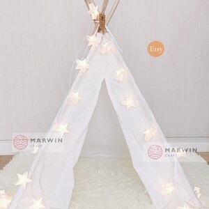 May include: White teepee tent with a string of white star-shaped lights draped around it. The teepee is on a white fluffy rug. The text "Marwin Craft" is visible on the left and right sides of the image. The text "Etsy" is visible in the upper right corner of the image.