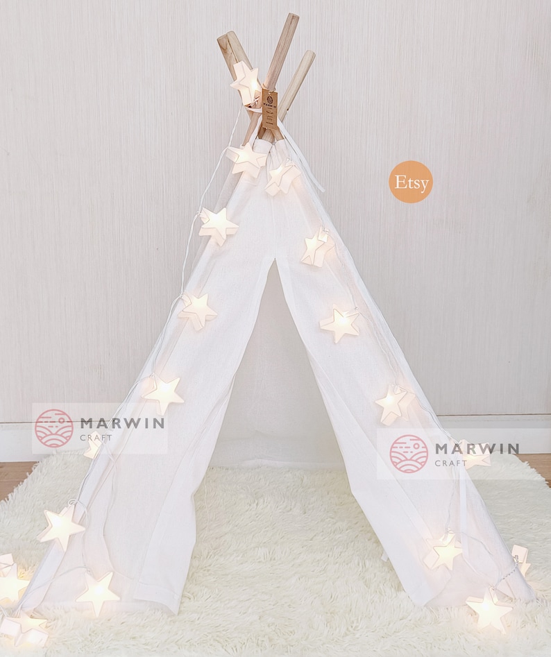 May include: White teepee tent with a string of white star-shaped lights draped around it. The teepee is on a white fluffy rug. The text "Marwin Craft" is visible on the left and right sides of the image. The text "Etsy" is visible in the upper right corner of the image.