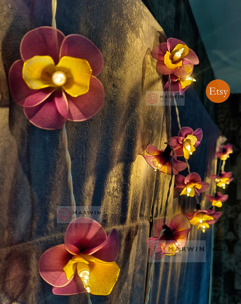 Puede incluir: Una cadena de luces con bombillas en forma de flores moradas y amarillas. Las luces est&aacute;n enhebradas en un cable y est&aacute;n encendidas. Las flores est&aacute;n hechas de tela y tienen un aspecto delicado y femenino. Las luces son perfectas para agregar un toque de fantas&iacute;a y romance a cualquier espacio.