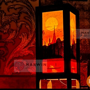 May include: A wooden lampshade with a stained glass design depicting a cityscape at sunset. The lampshade is lit from within, casting a warm glow. The text "MARWIN CRAFT" is visible on the lampshade.