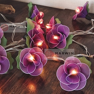 May include: Purple flower string lights with warm white LED bulbs. The lights are strung on a clear wire and are perfect for adding a touch of whimsy to any space.