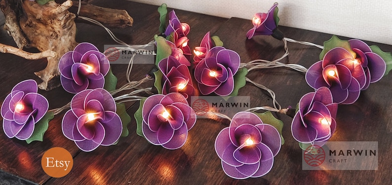 May include: Purple flower string lights with warm white LED bulbs. The lights are strung on a clear wire and are perfect for adding a touch of whimsy to any space.