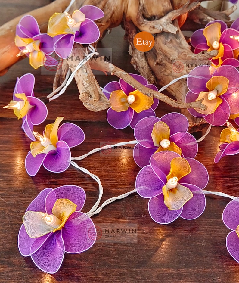 Puede incluir: Una cadena de luces con bombillas en forma de flor de color morado y amarillo. Las luces est&aacute;n enhebradas en un cable blanco y est&aacute;n encendidas. Las flores est&aacute;n hechas de tela y tienen un aspecto delicado y femenino. Las luces son perfectas para agregar un toque de fantas&iacute;a y encanto a cualquier espacio.