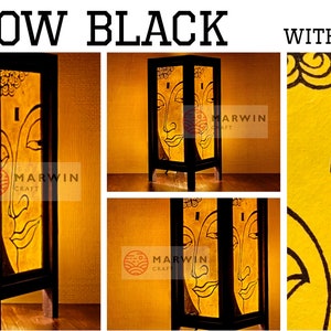 May include: A yellow and black table lamp with a gold foil accent. The lamp features a Buddha face design and is made of wood. The lamp is lit and the light shines through the paper.
