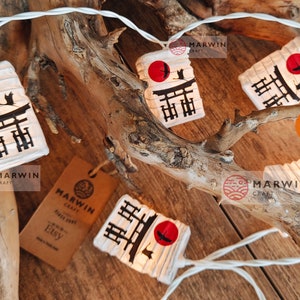 K&ouml;nnte beinhalten: Lichterkette mit wei&szlig;en Lichtern und Papierlaternen mit einem japanischen Tempeltor und einem roten Sonnenmotiv. Die Laternen sind an einem Ast befestigt und haben ein wei&szlig;es Kabel. Der Text "Marwin Craft" und "Etsy" ist auf dem Bild zu sehen.