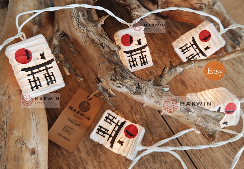 K&ouml;nnte beinhalten: Lichterkette mit wei&szlig;en Lichtern und Papierlaternen mit einem japanischen Tempeltor und einem roten Sonnenmotiv. Die Laternen sind an einem Ast befestigt und haben ein wei&szlig;es Kabel. Der Text "Marwin Craft" und "Etsy" ist auf dem Bild zu sehen.