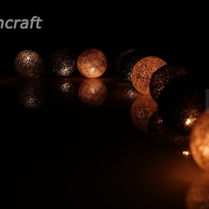 Puede incluir: Una cadena de luces de bola de algodón blanco cálido con un brillo sutil. Las luces están enhebradas en una línea curva y emiten un brillo suave.