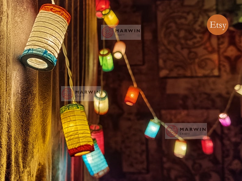 May include: String of colorful paper lanterns, each with a unique shape and hue, including red, yellow, blue, and green. The lanterns are strung together on a white wire, creating a festive and decorative lighting display.