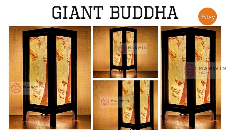 May include: A wooden table lamp with a light brown shade featuring a stylized image of a Buddha. The lamp has a black base and a black cord. The lamp is lit and casting a warm glow. The lamp is labeled "Marwin Craft" and "Etsy".