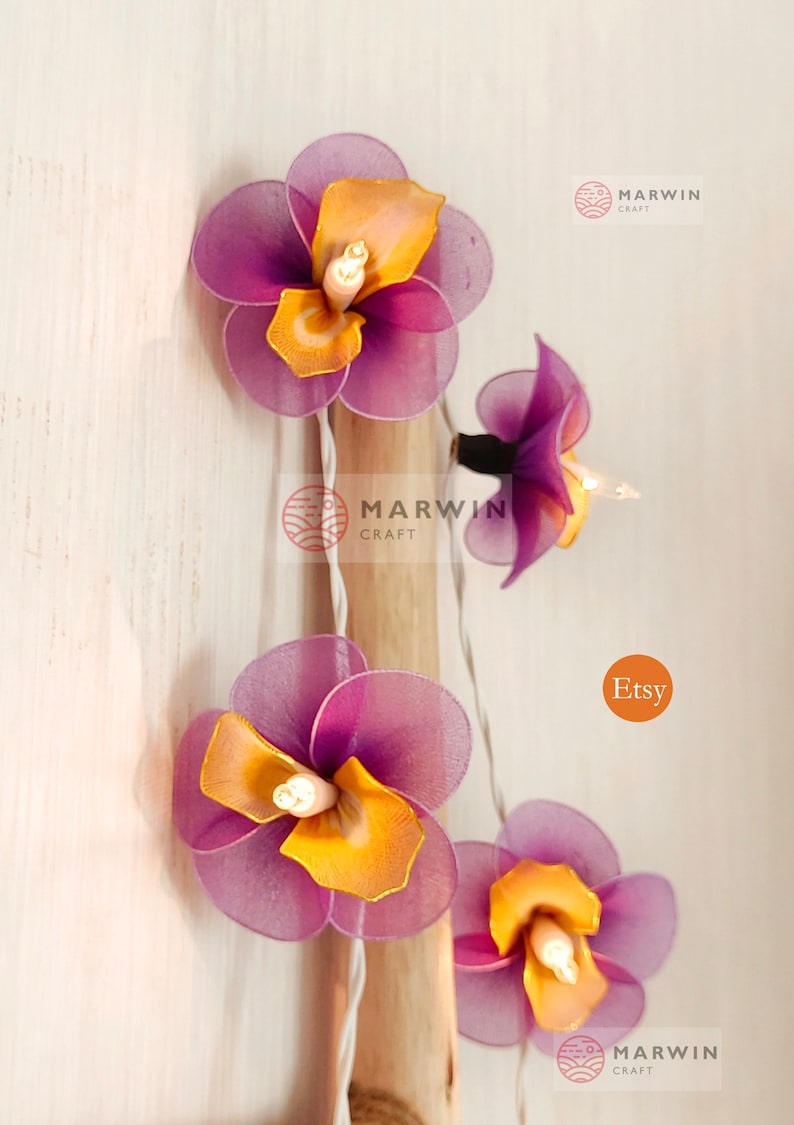 Puede incluir: Una cadena de luces con bombillas en forma de flores de color morado y amarillo. Las luces est&aacute;n enhebradas en un cable blanco y est&aacute;n encendidas. Las flores est&aacute;n hechas de tela y tienen un aspecto delicado y femenino. Las luces son perfectas para a&ntilde;adir un toque de fantas&iacute;a y encanto a cualquier espacio.